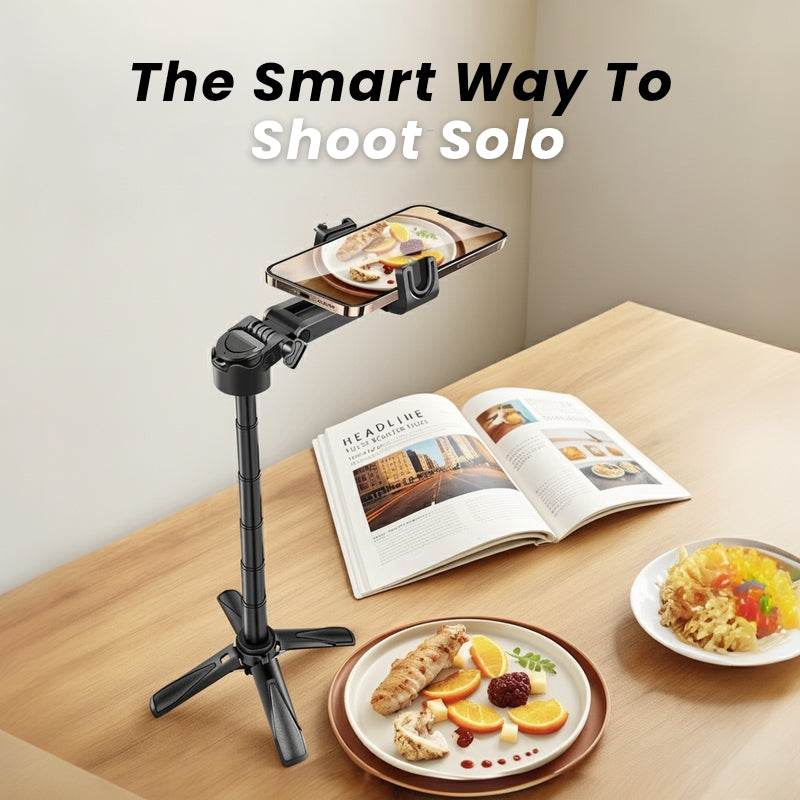 Smart phone holder on a tripod with plates of food and an open magazine on a table.